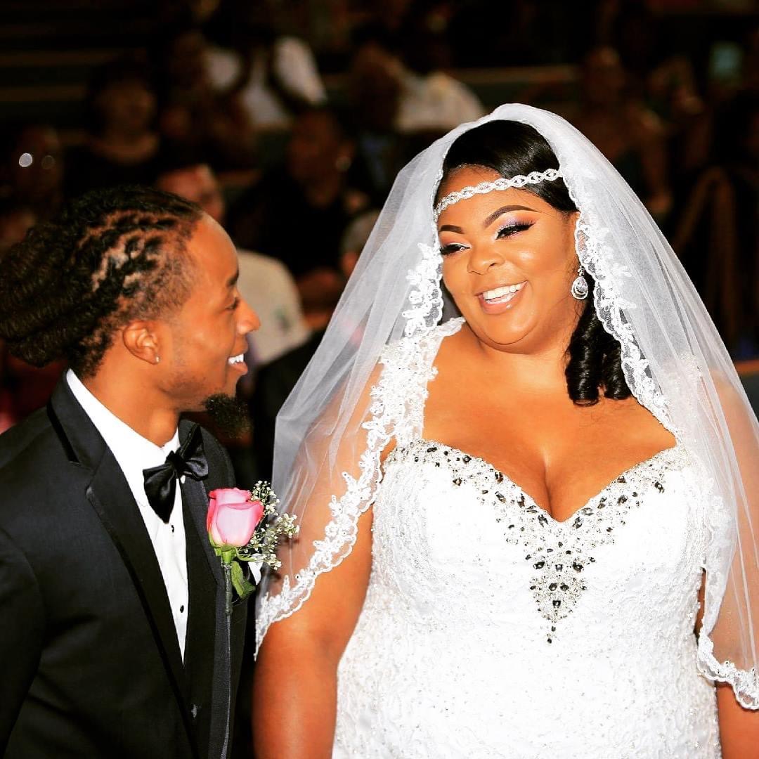Bride and groom smiling at each other during wedding ceremony, bride in white dress with veil, groom in tuxedo with boutonniere.