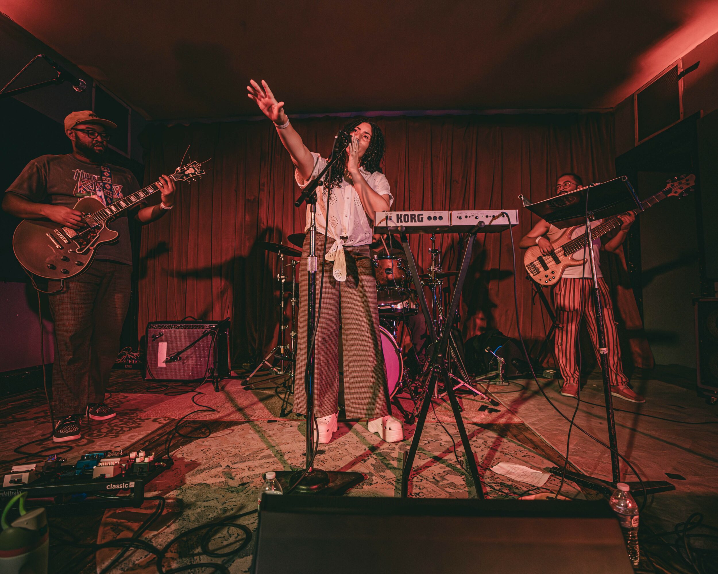Band performing on stage with a singer, guitarist, bassist, and keyboardist, in a dimly lit venue with red curtains.