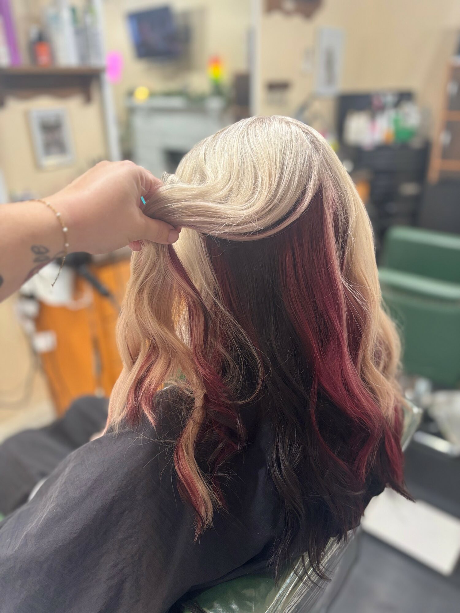 Person's hair with blonde, pink, and purple colors, held by hand, in a salon setting.
