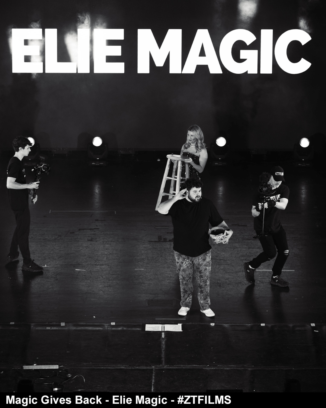 Four people on stage with large text 'ELLE MAGIC' above, one person with a ladder, others holding objects, in black and white.