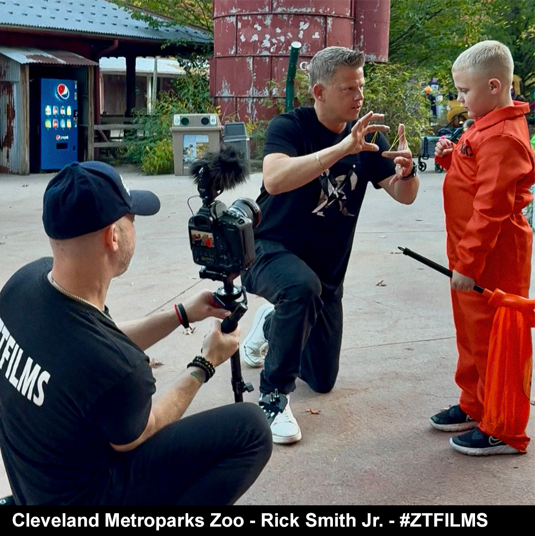 Man kneeling and taking a photo of a boy in an orange jumpsuit at Cleveland Metroparks Zoo.