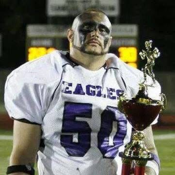 Football player in uniform holding a trophy, wearing eye black, on a field at night.