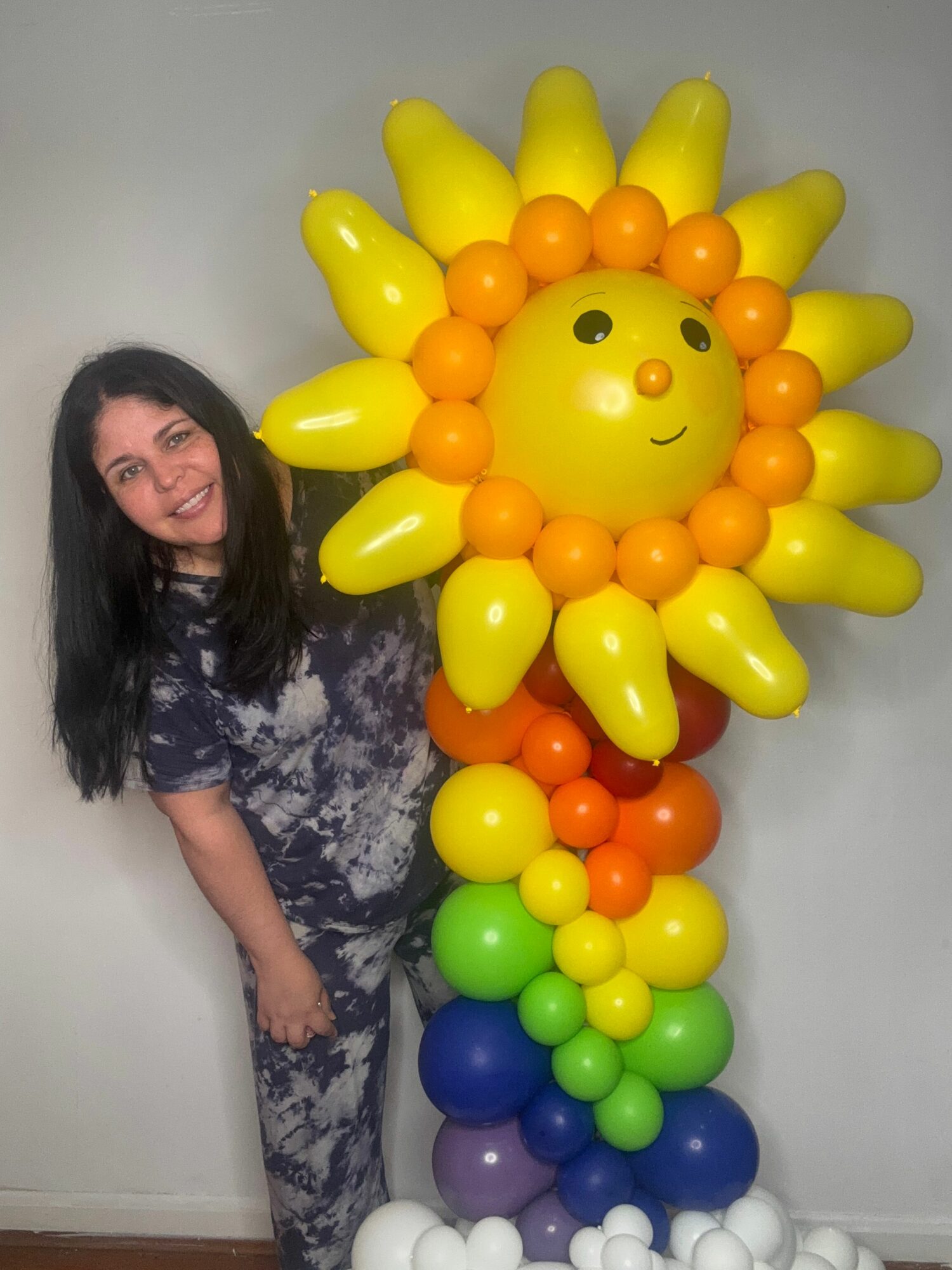 Person lying on a couch with a colorful balloon sculpture of a smiling sun and rainbow behind them.