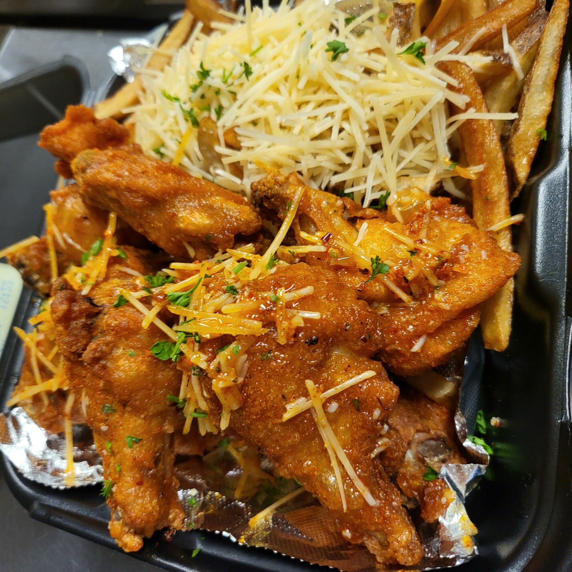 Fried chicken wings topped with shredded cheese and herbs, served with French fries and shredded cheese on top.