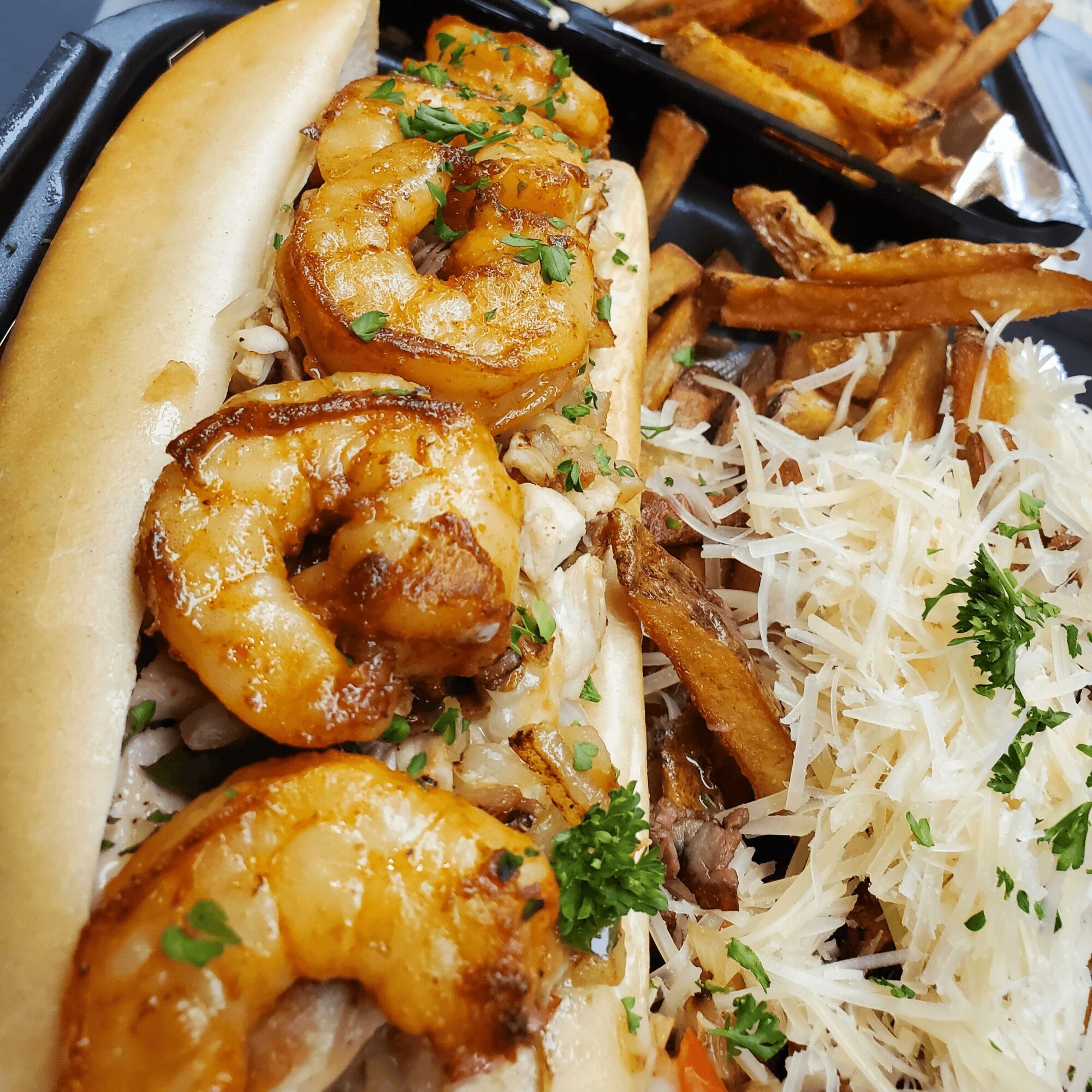 Shrimp po' boy sandwich with lettuce in a bun, served with shredded cheese and fries on the side.