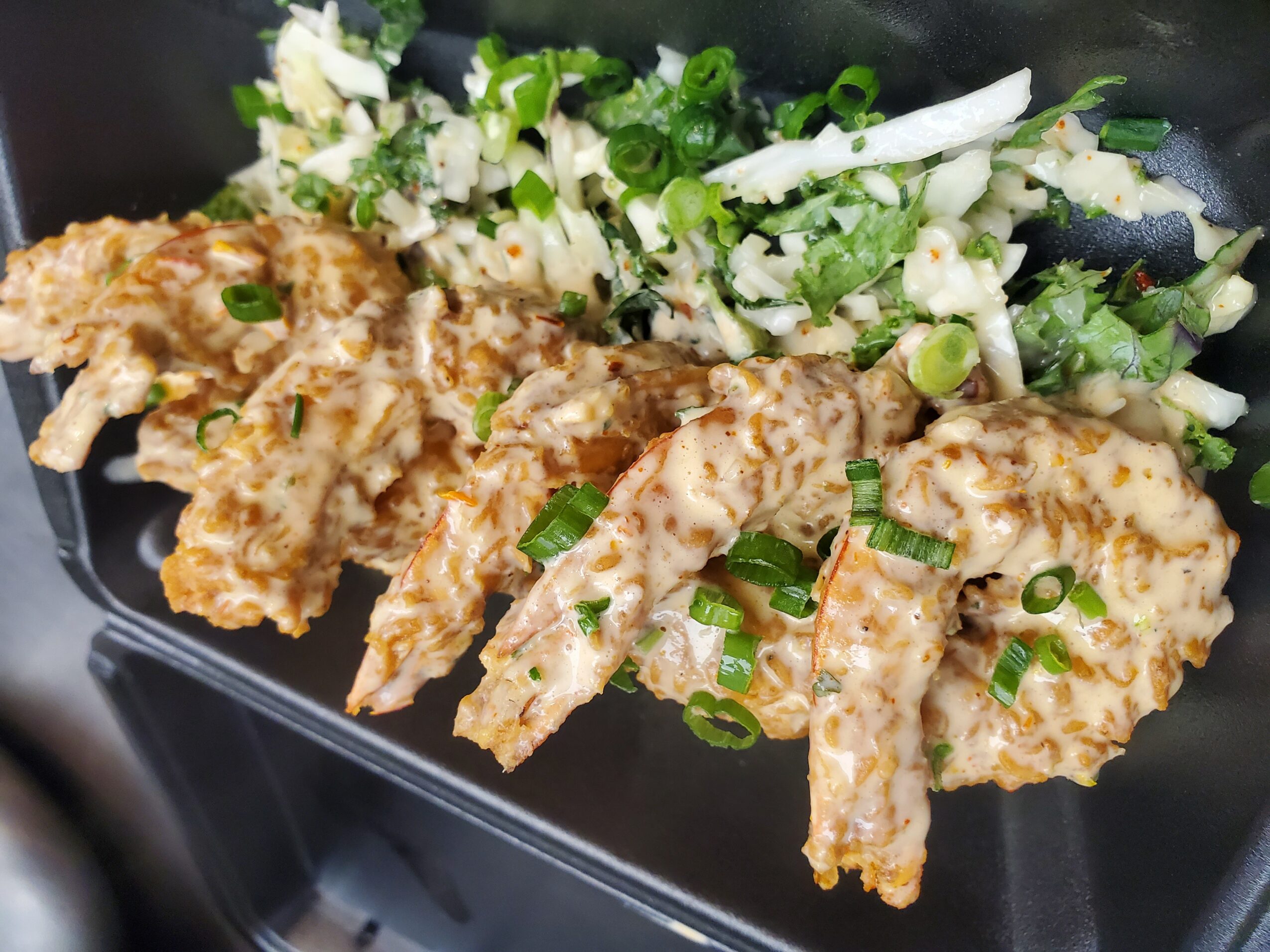 Fried fish fillets garnished with chopped green onions, served with a side of chopped vegetables, on a black plate.