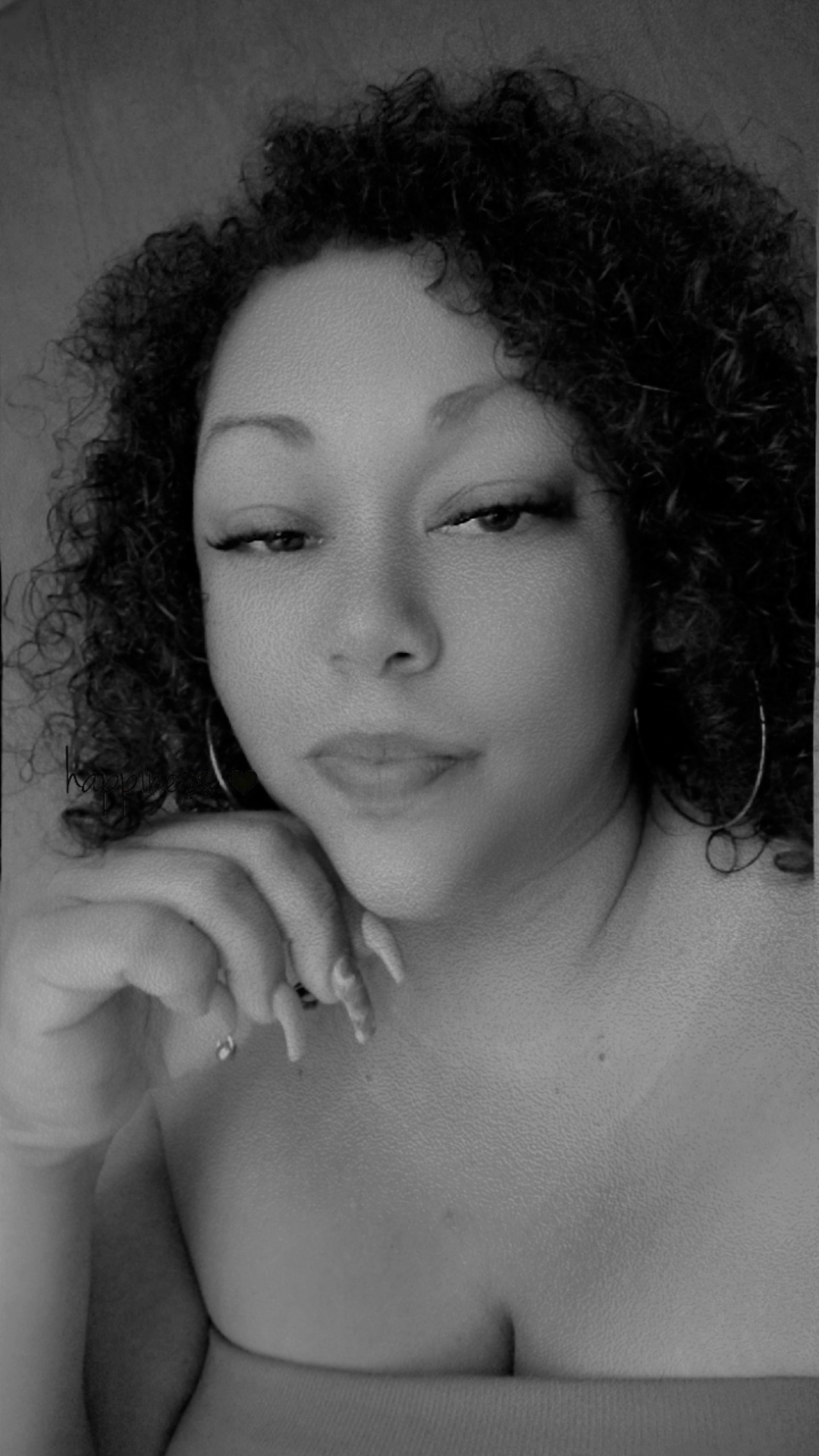 Woman with curly hair and hoop earrings, resting her chin on her hand, looking at the camera.