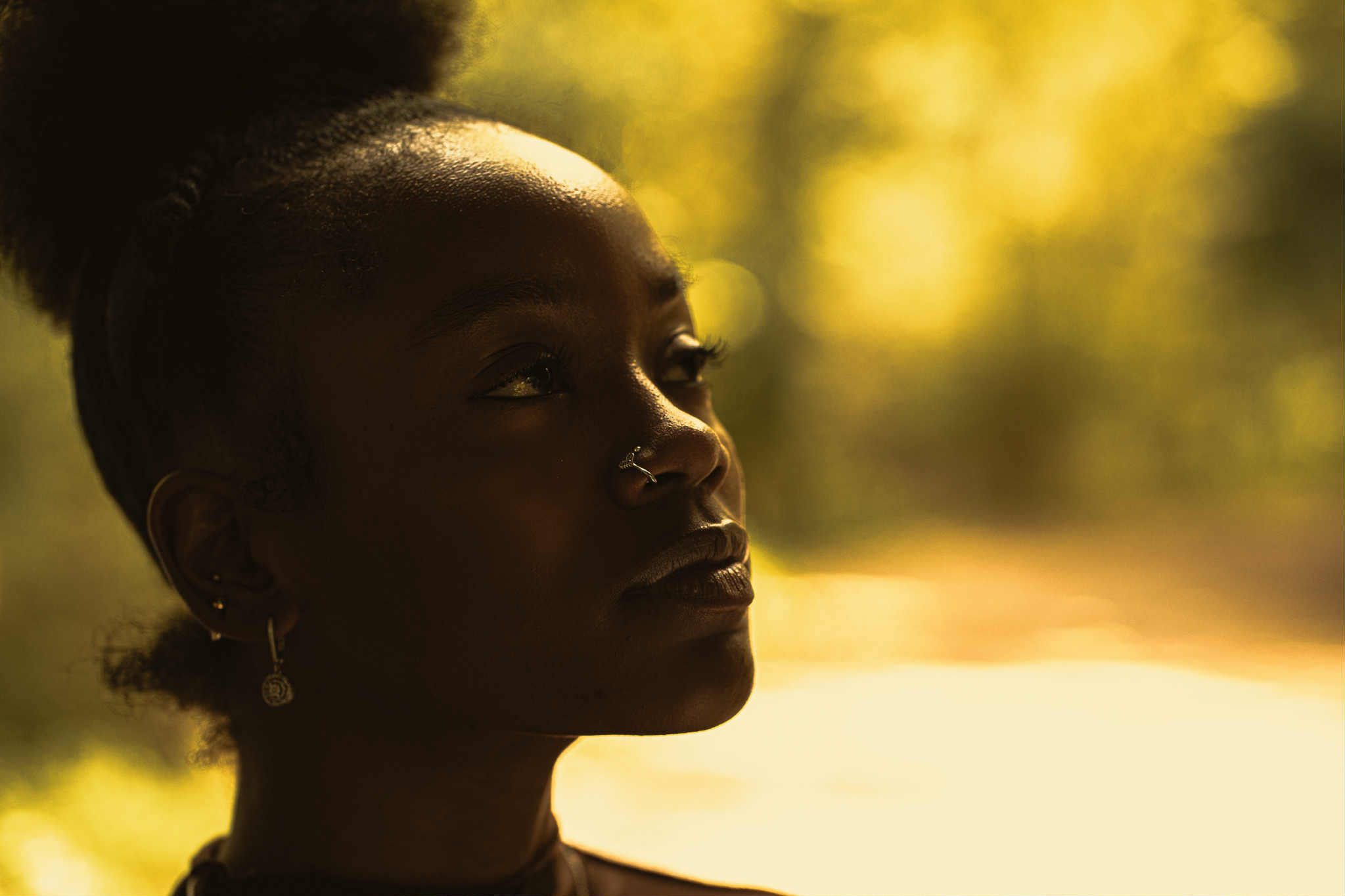 Portrait of a woman with dark skin and braided hair, outdoors with blurred yellow-green background.