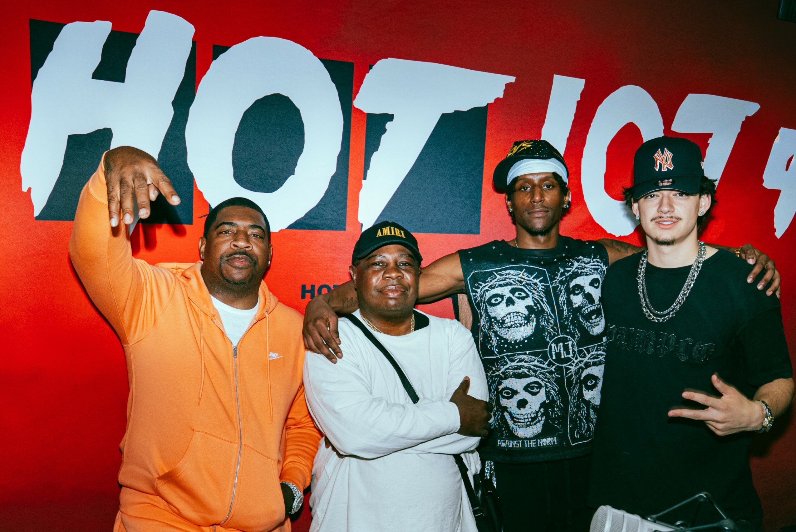 Four men stand together in front of a red background with large white text, posing for a photo.