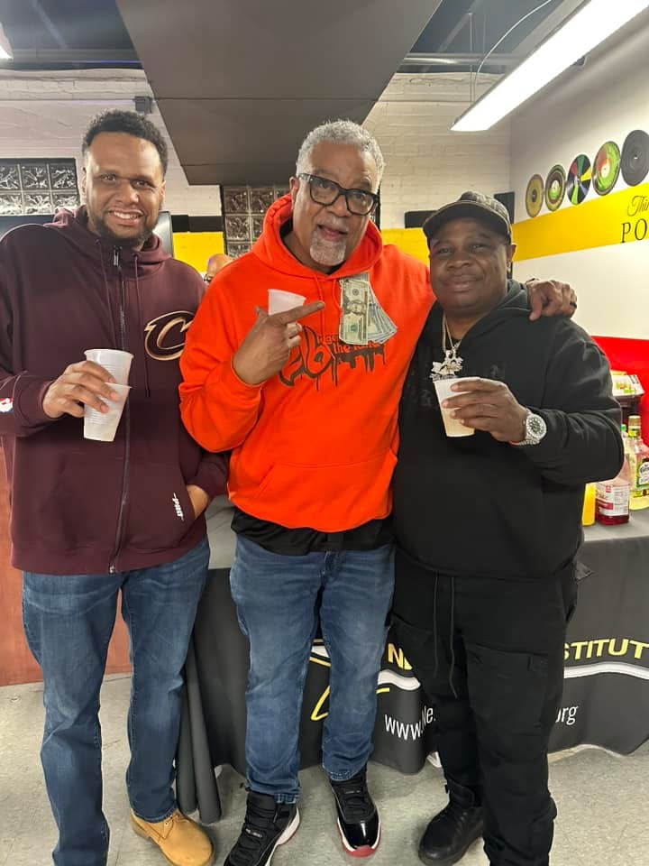 Three people smiling and holding drinks in a store, one person holding cash, all wearing casual clothing.
