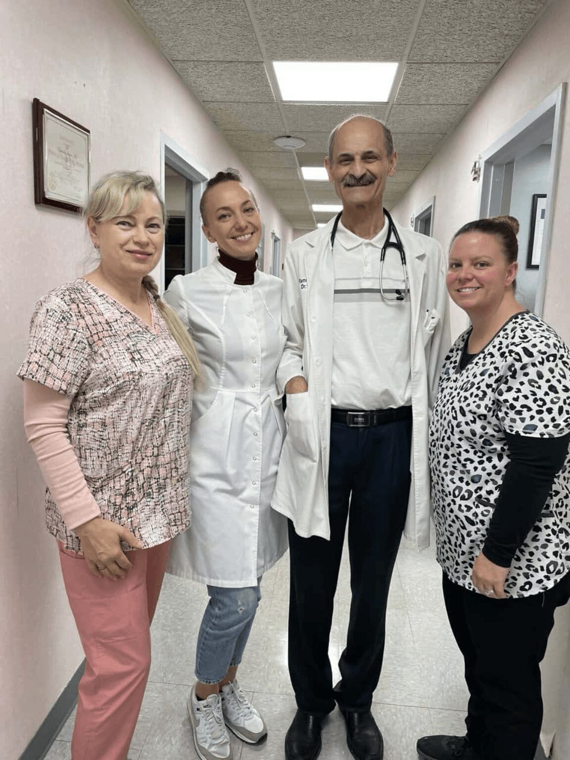 Four healthcare professionals standing in a hospital corridor, smiling, with two women on the left and two men on the right.