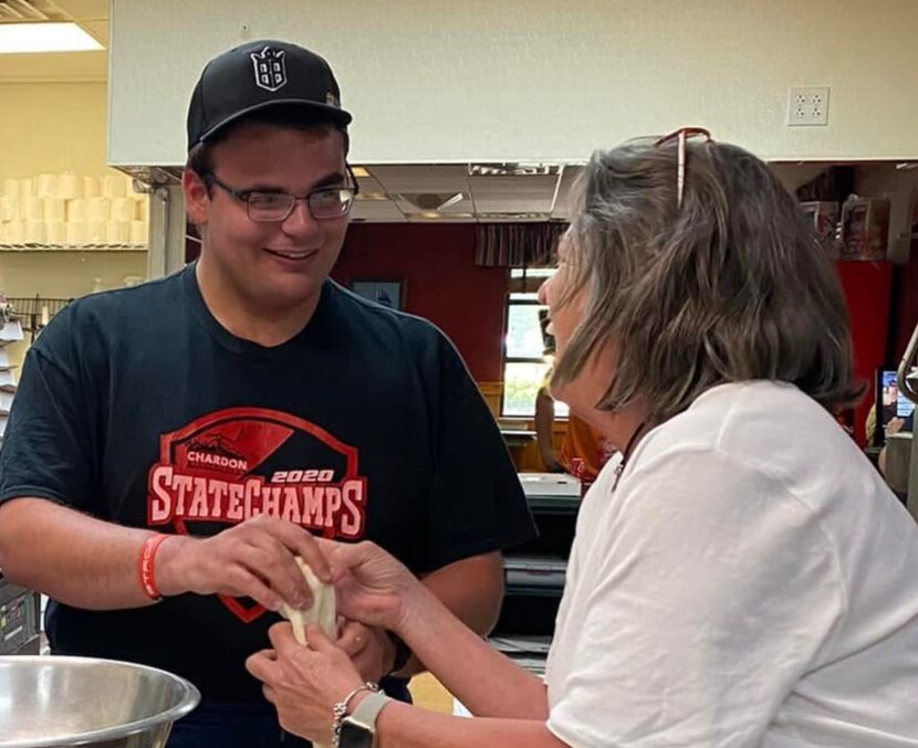 A young man and woman are exchanging money or tickets indoors, with shelves and a counter in the background.