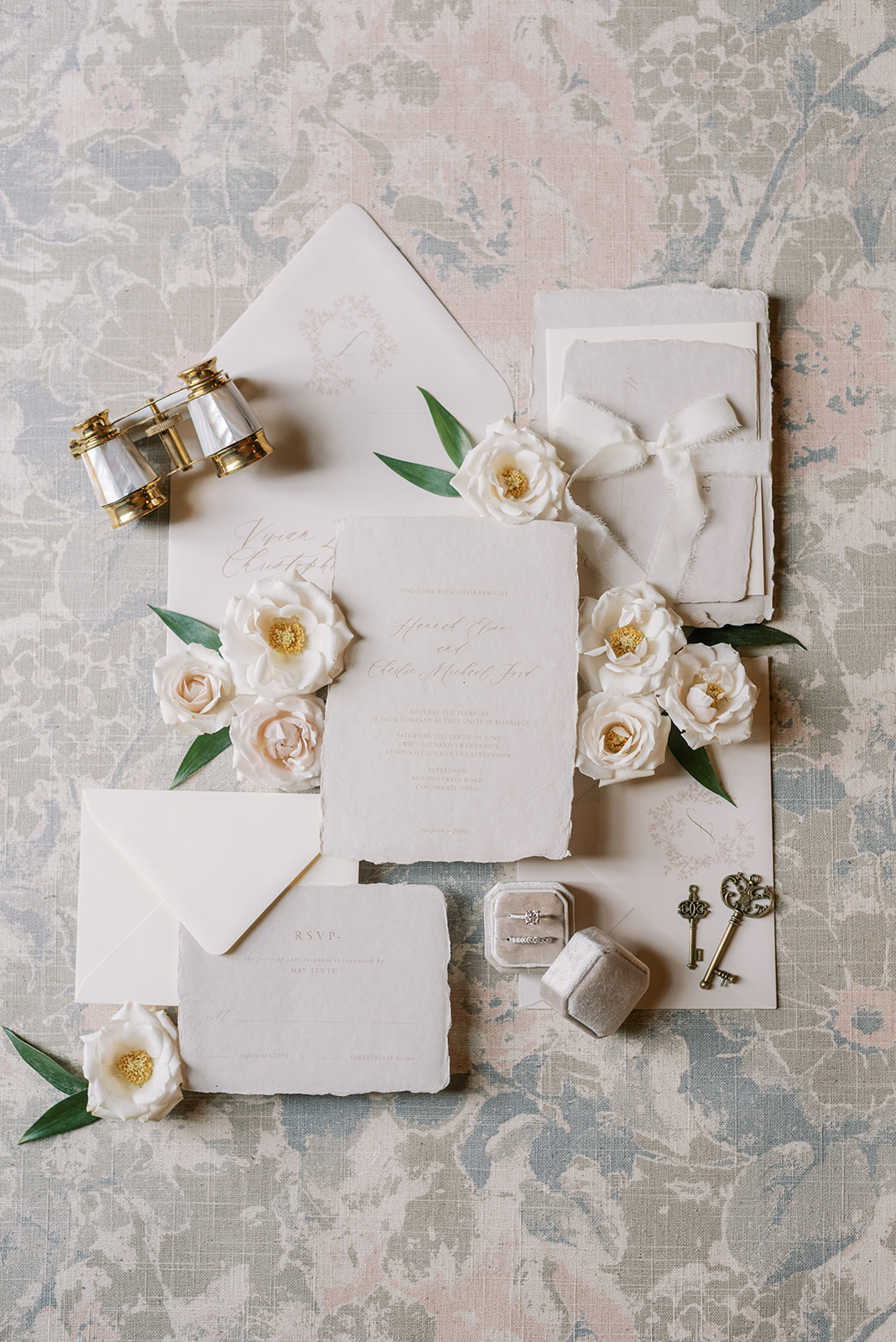 Flat lay of wedding items including rings, flowers, envelopes, and a key on a textured surface.