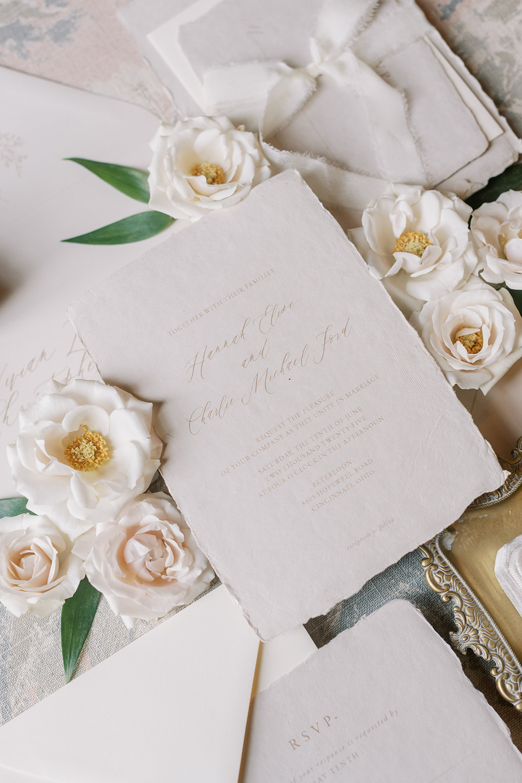 Invitation card surrounded by white and blush roses with green leaves, on a textured surface.
