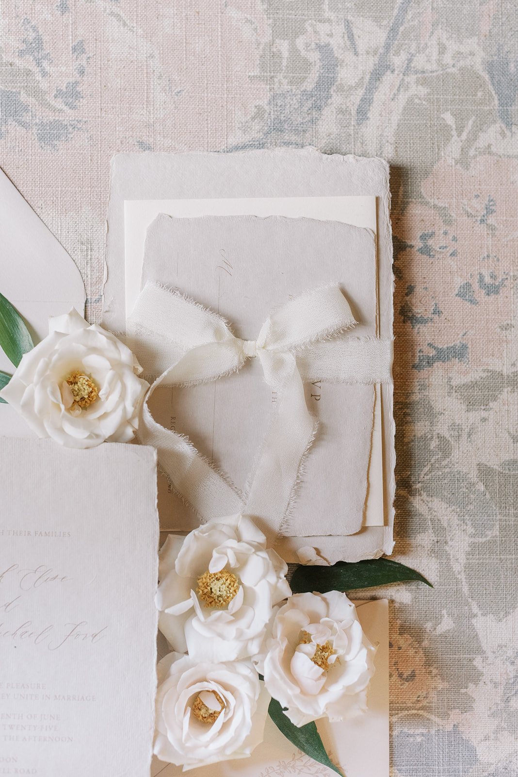 White flowers with green leaves on a textured surface, with a white card or paper behind them.