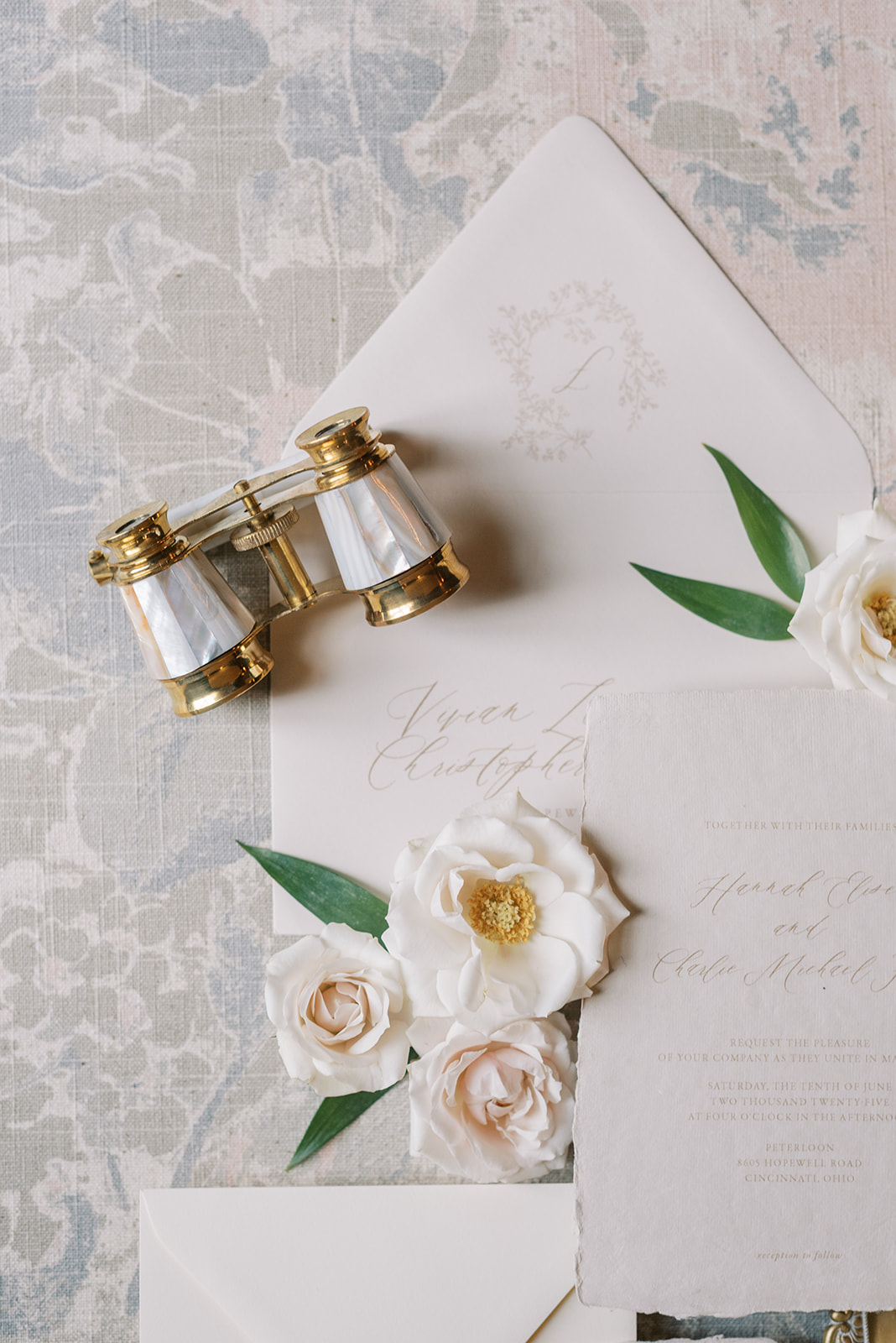 Open letter with white flowers and green leaves, vintage binoculars, and a notebook on a textured surface