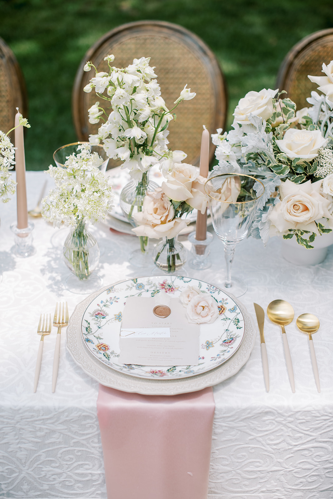Elegant table setting with floral arrangements, candles, and gold cutlery on a white tablecloth, with chairs in the background.