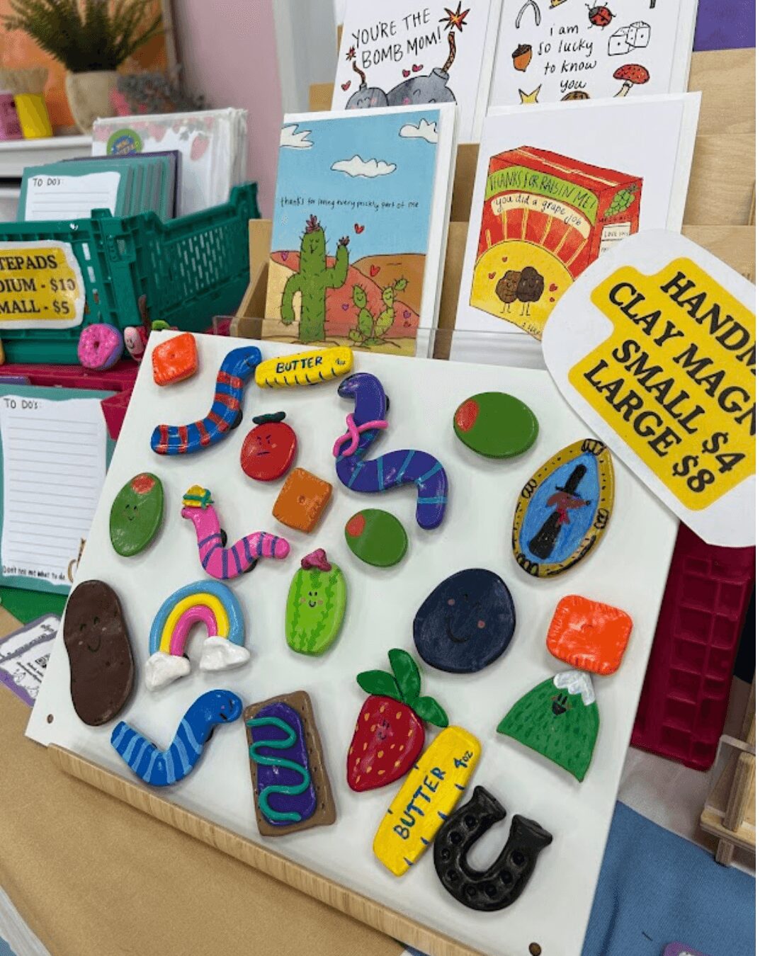 Display of colorful soap bars shaped like animals and objects on a white surface, with books and signs in the background.