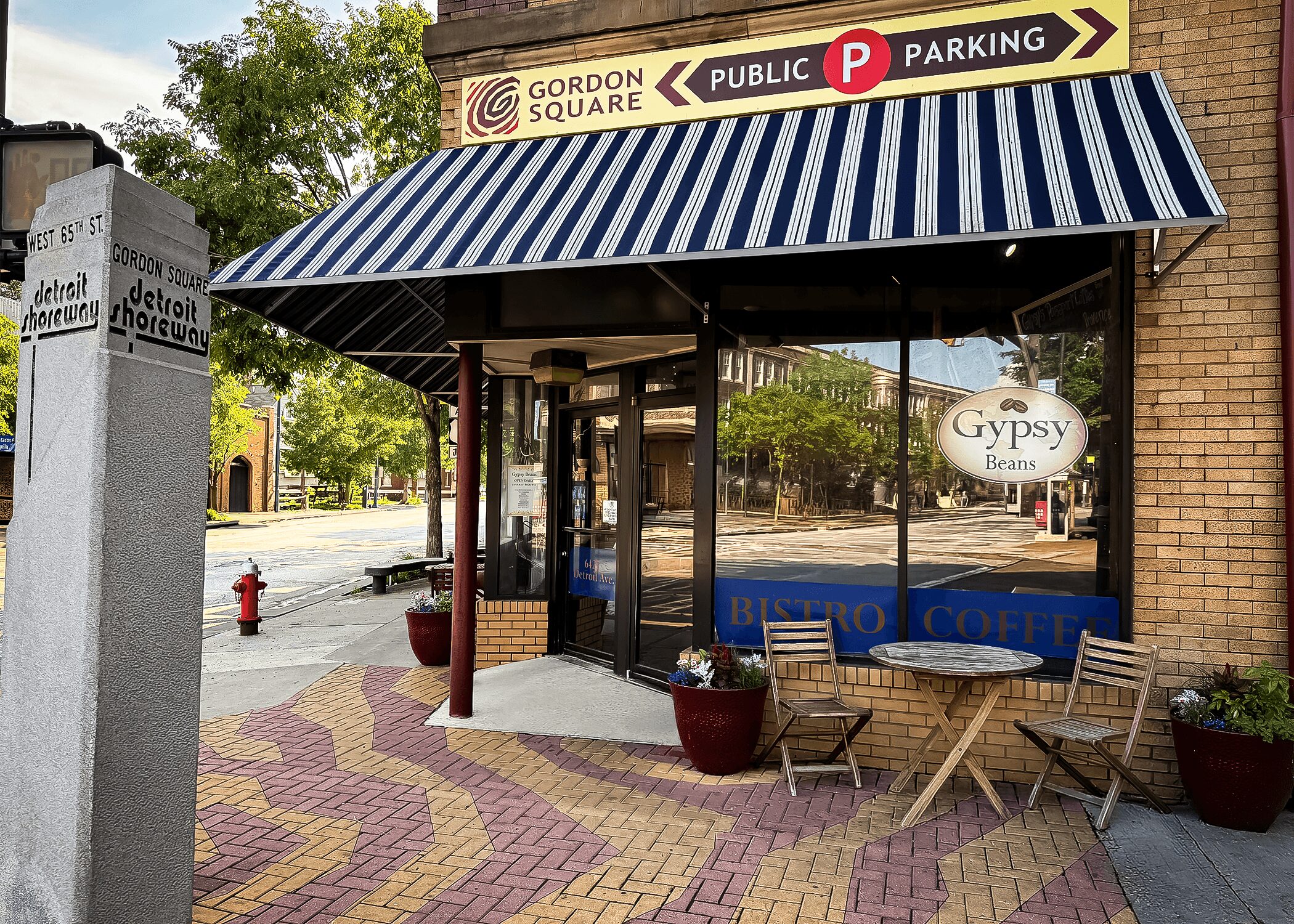 Cafe entrance with striped awning, outdoor seating, and a sign for Gypsy Bean coffee, on a brick building corner.