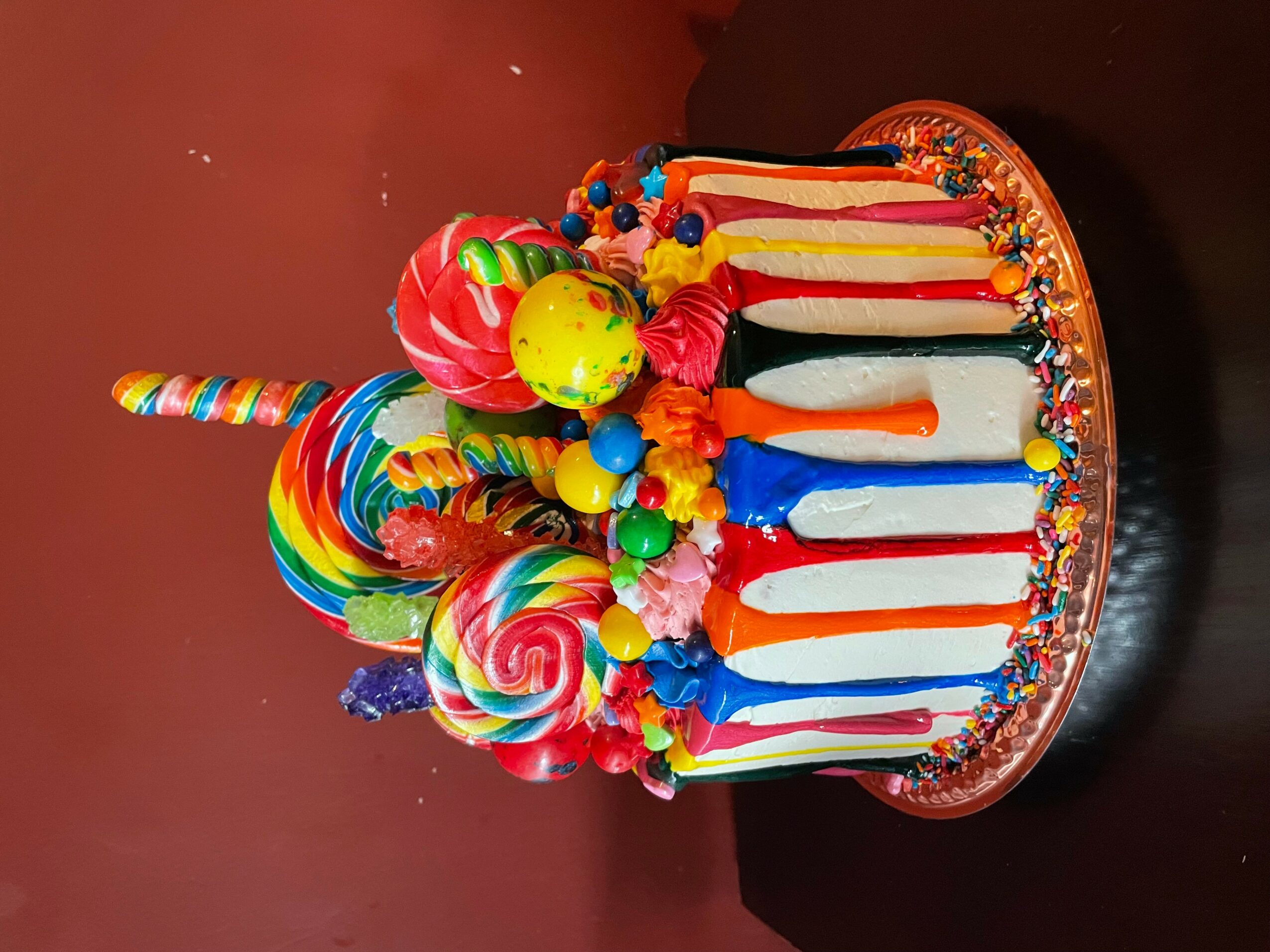 Colorful birthday cake with candies, lollipops, and candles on top, decorated with bright colors and sprinkles.