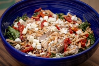Salad with shredded chicken, chopped vegetables, cheese, and greens in a blue bowl.