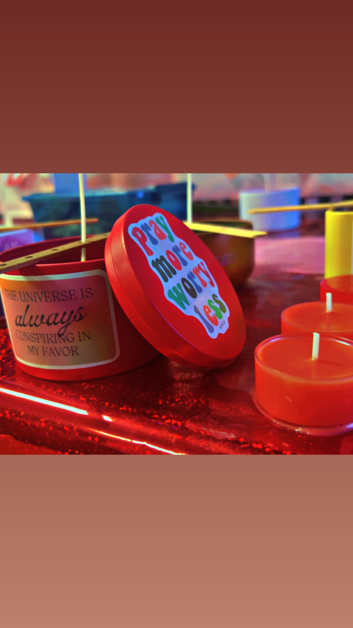 Red container with a colorful sticker, surrounded by orange and yellow candles, on a red surface.