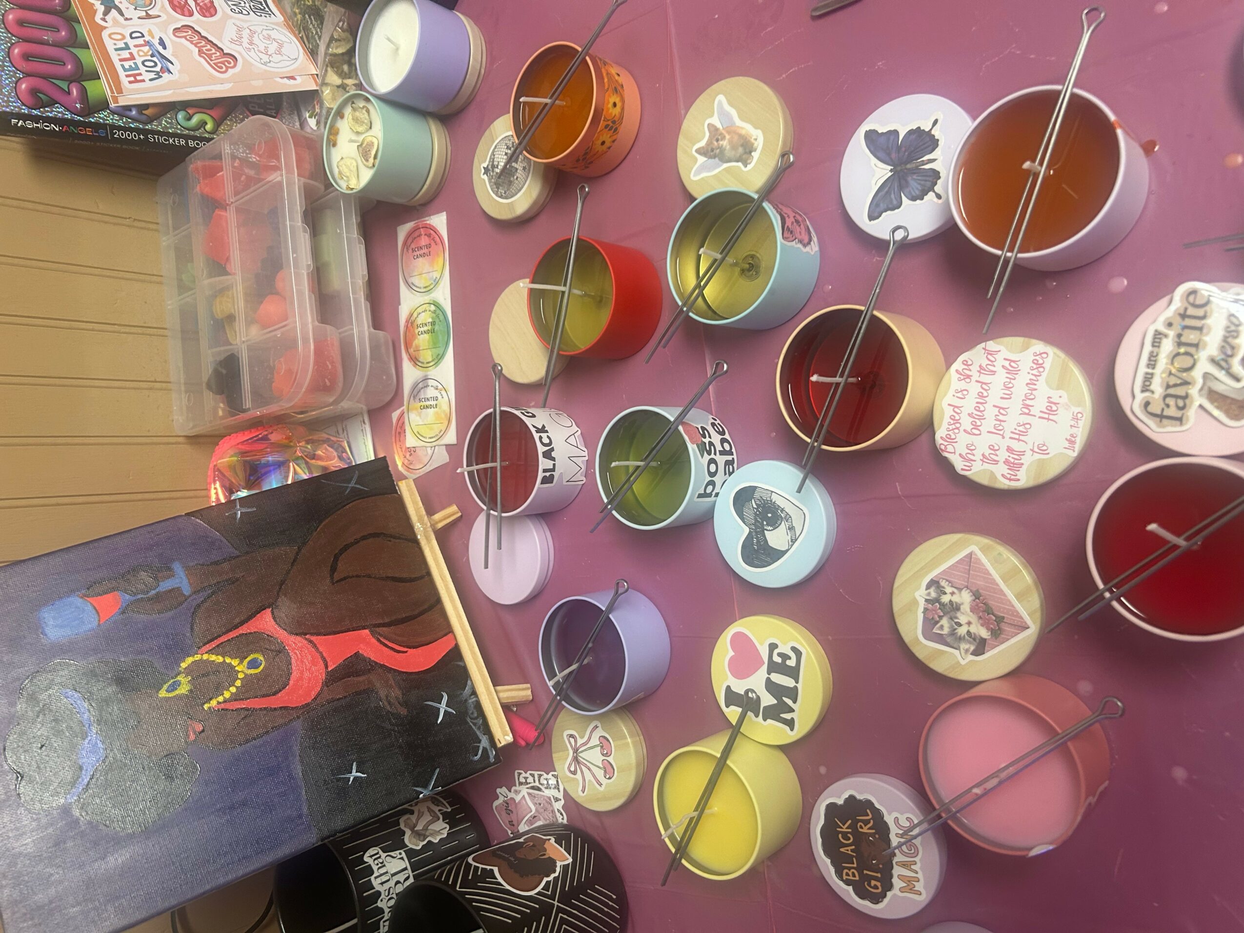 Colorful small containers with sticks, some with labels, on a pink surface, alongside a partially visible book or box.