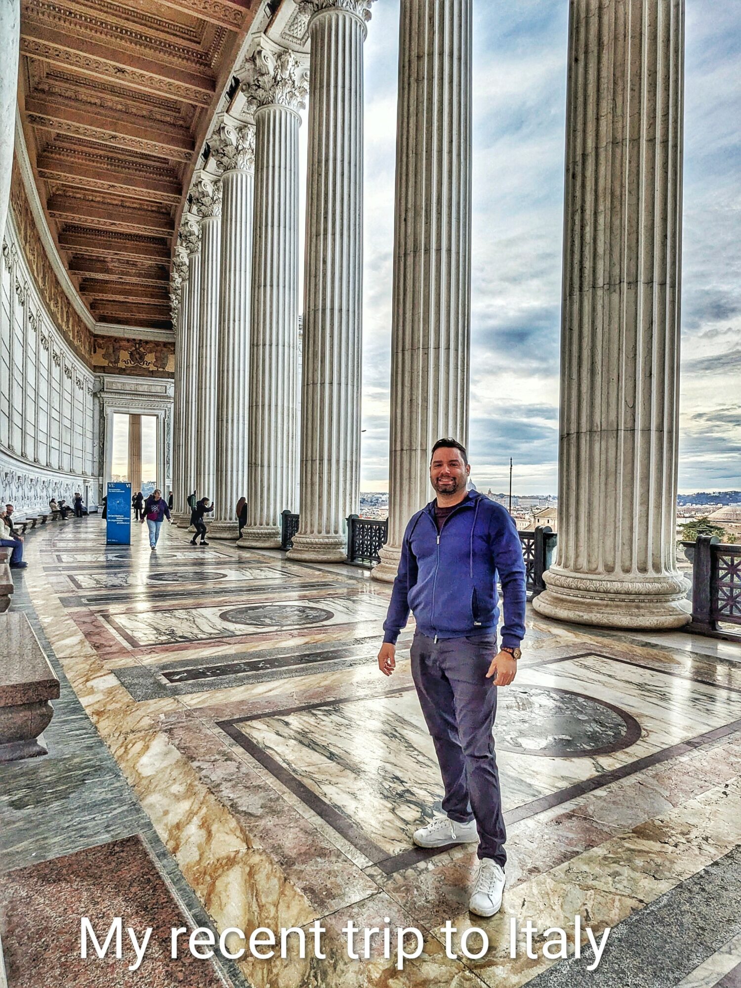Man standing among tall columns with a cloudy sky background, marble floor beneath him, in a historic building in Italy.