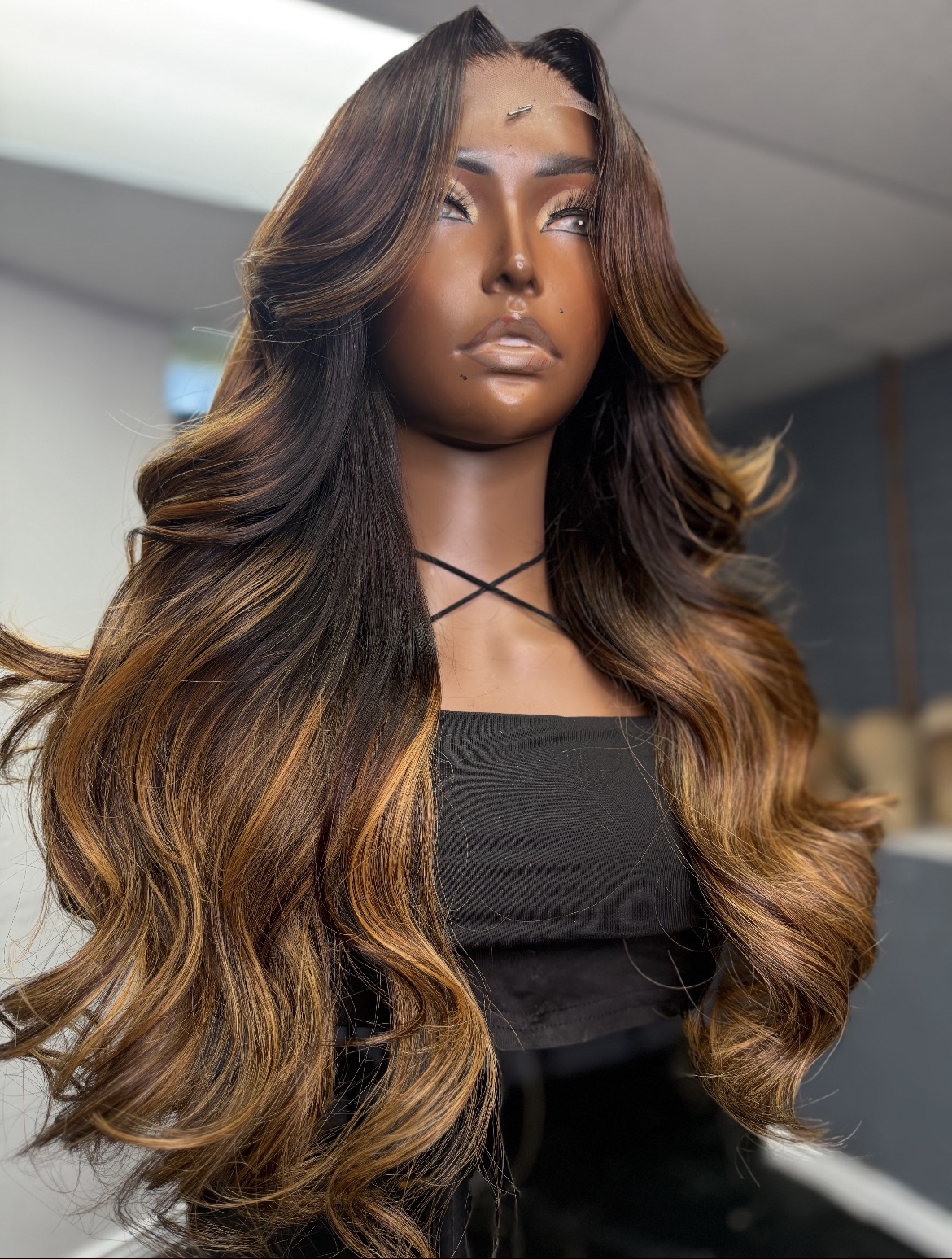 Woman with long, wavy hair and makeup, wearing a black top, looking to the side in an indoor setting.