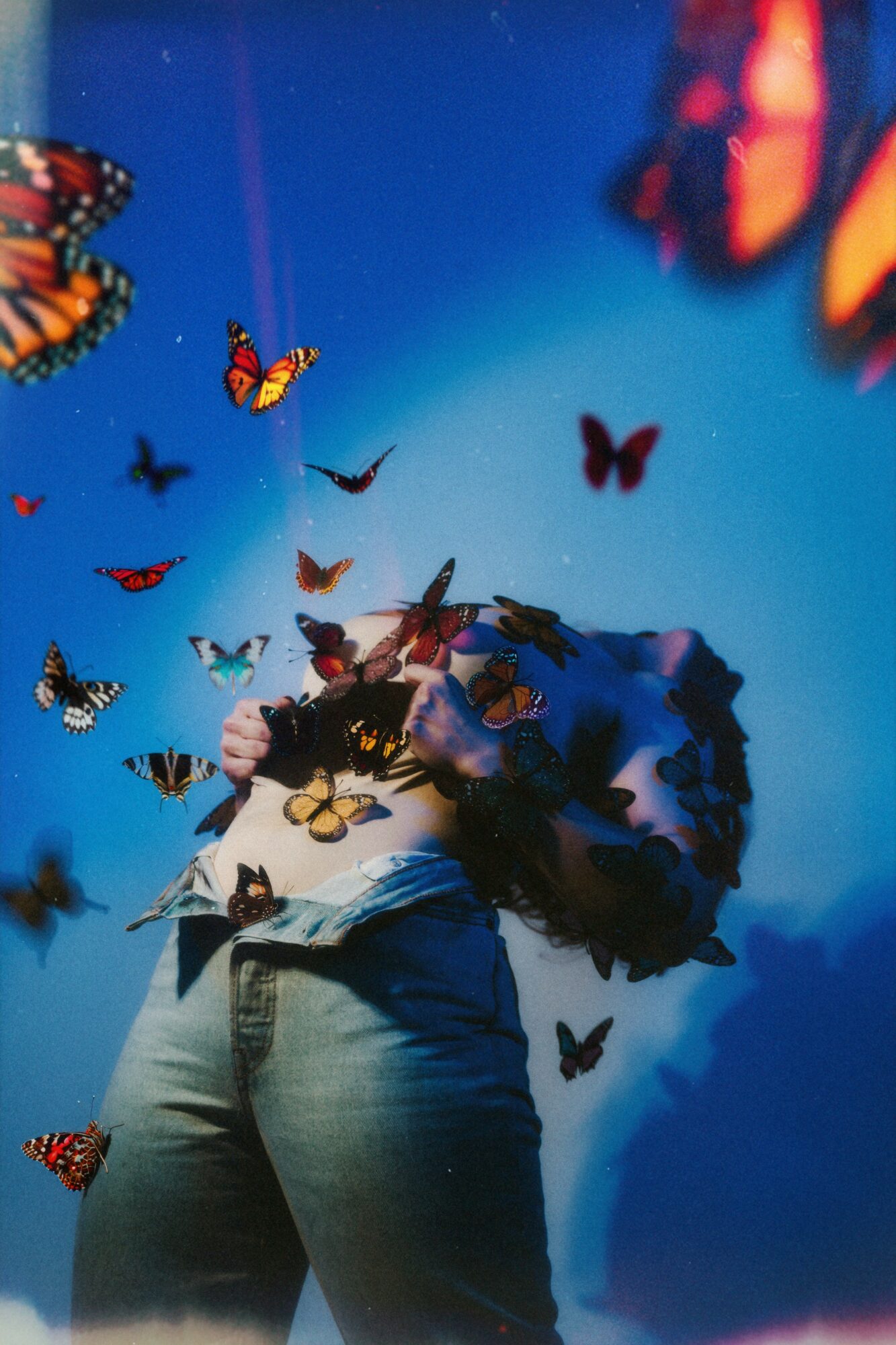 Person standing with arms crossed, surrounded by flying butterflies against a blue background.