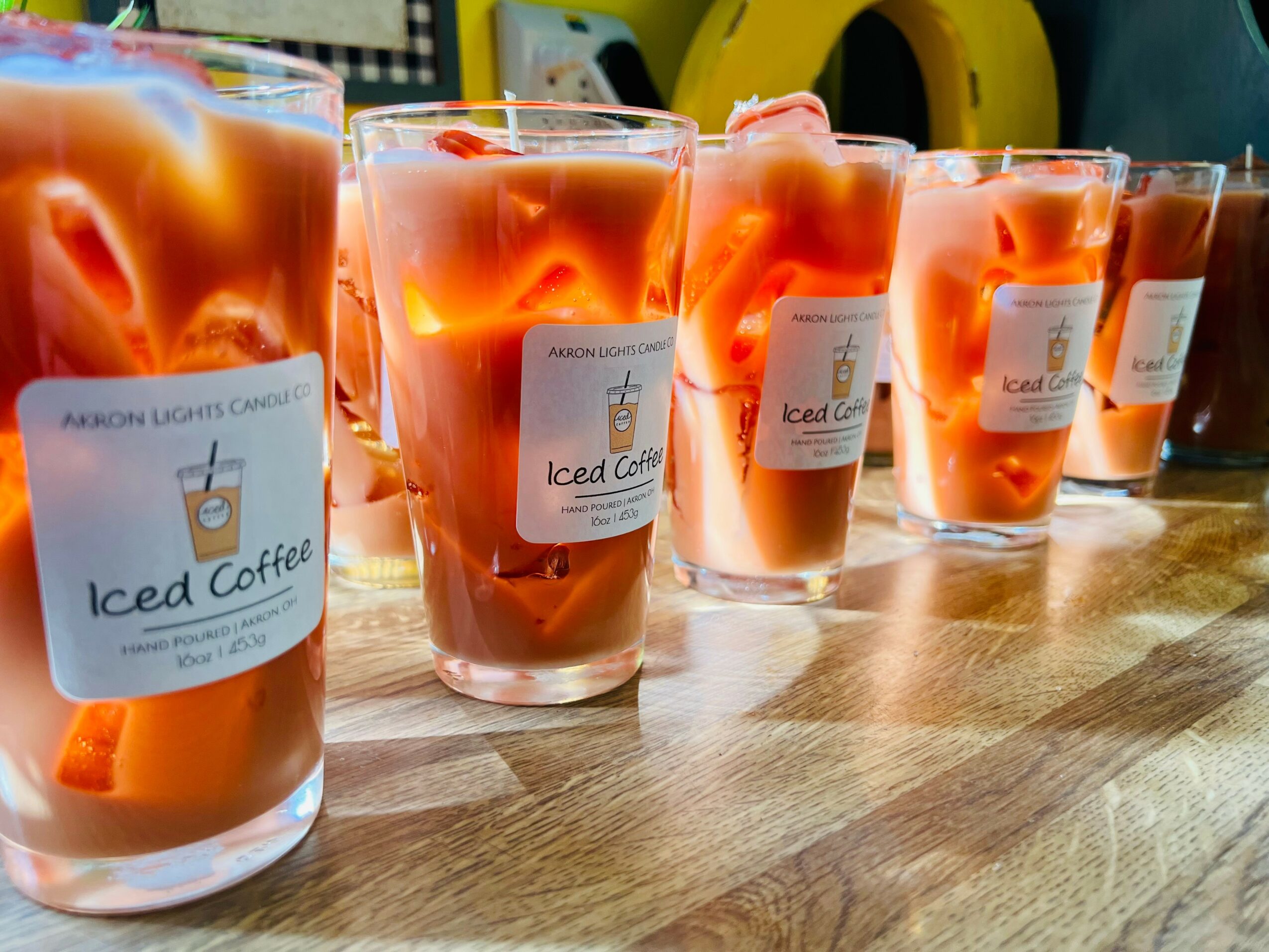 Six glasses of iced coffee with orange-colored liquid on a wooden surface, with a blurred background.