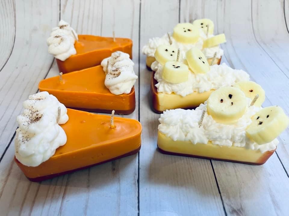 Four decorated desserts on a wooden surface, two with orange glaze and whipped cream, two with white base and banana slices, some with faces