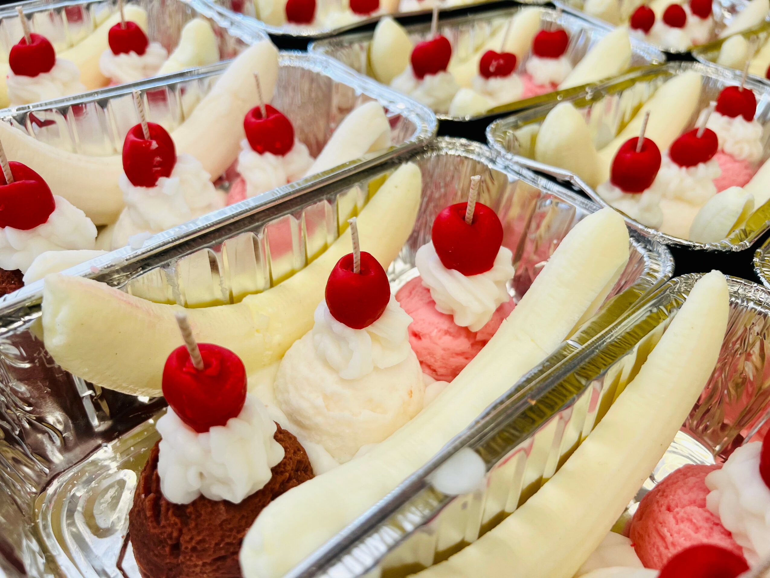 Assorted desserts in clear containers with cherries, white chocolate, and pink and brown toppings, arranged in rows.
