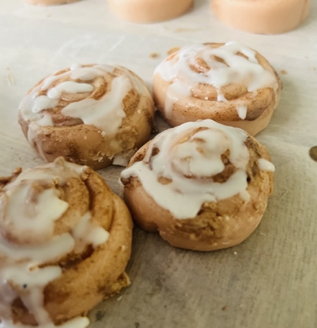 Four cinnamon rolls with icing on a parchment paper surface, close-up view.