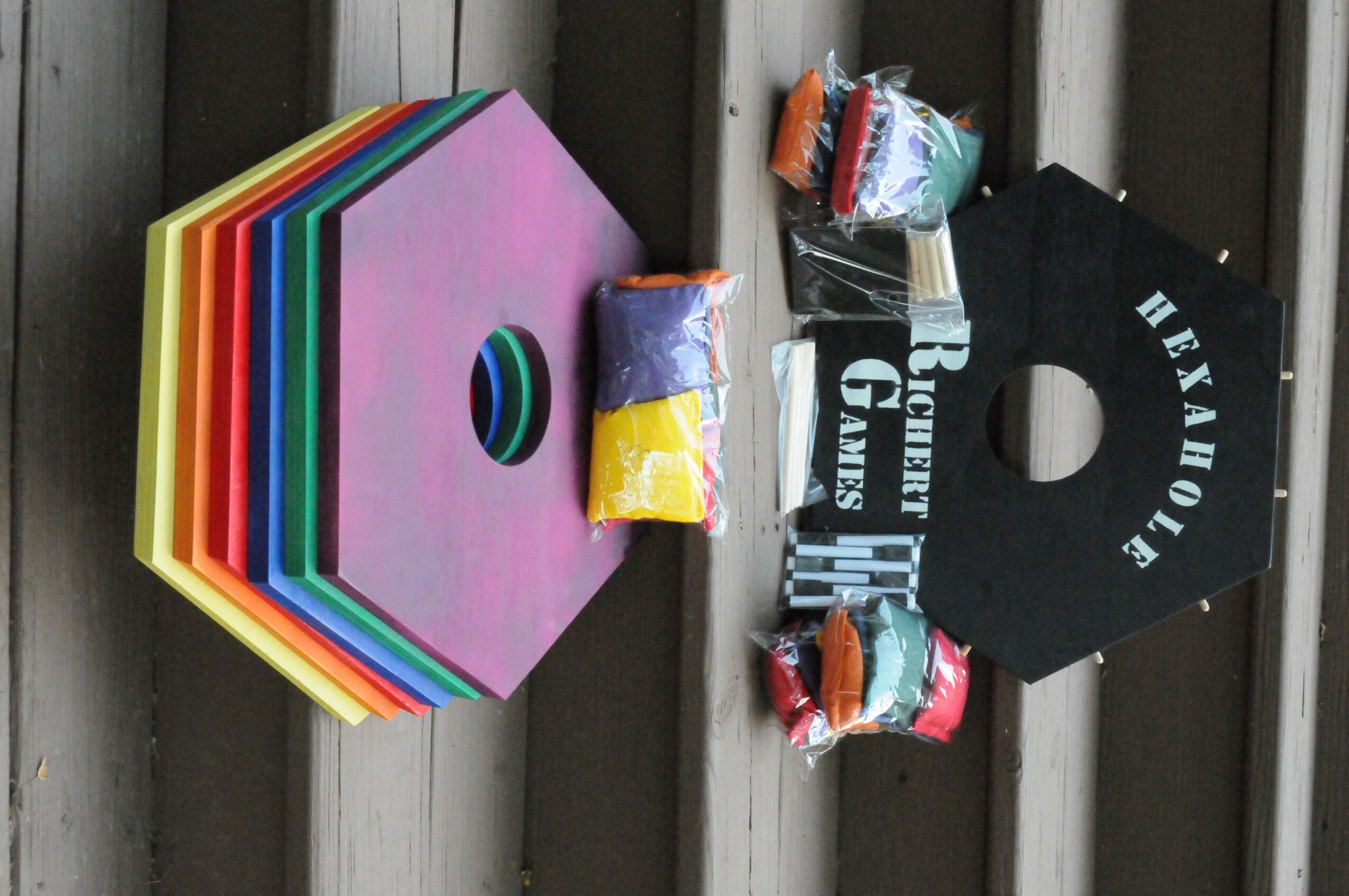 Colorful hexagonal game piece, small wrapped candies, and a black tag with white text on a wooden surface.