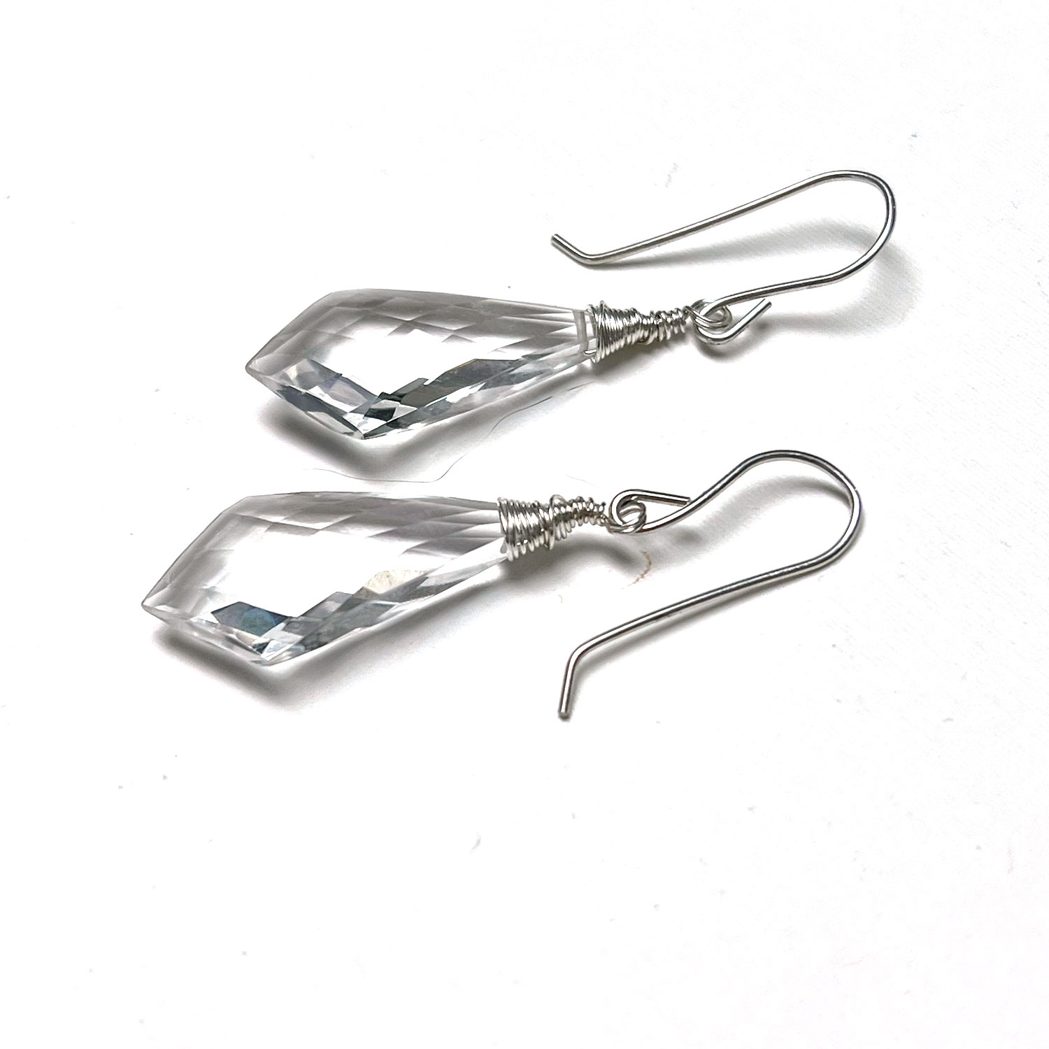Pair of clear, faceted teardrop-shaped earrings with metal hooks, lying flat on a white background.