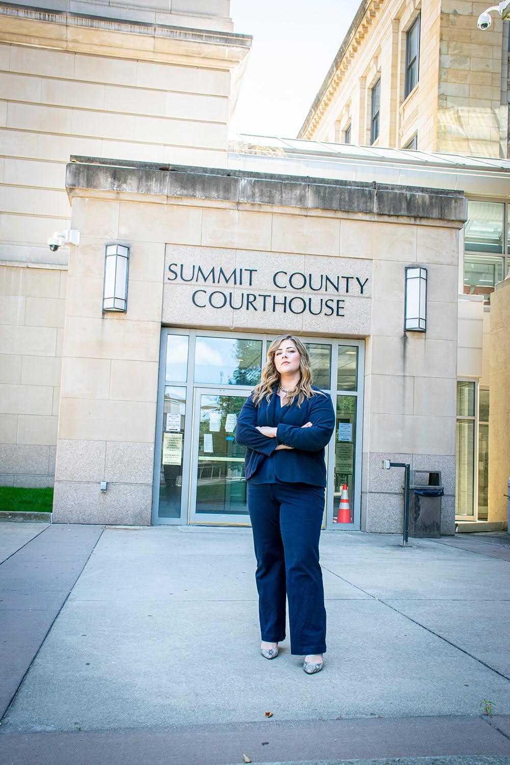 Woman standing with arms crossed in front of Summit County Courthouse entrance, building with stone facade and glass doors.