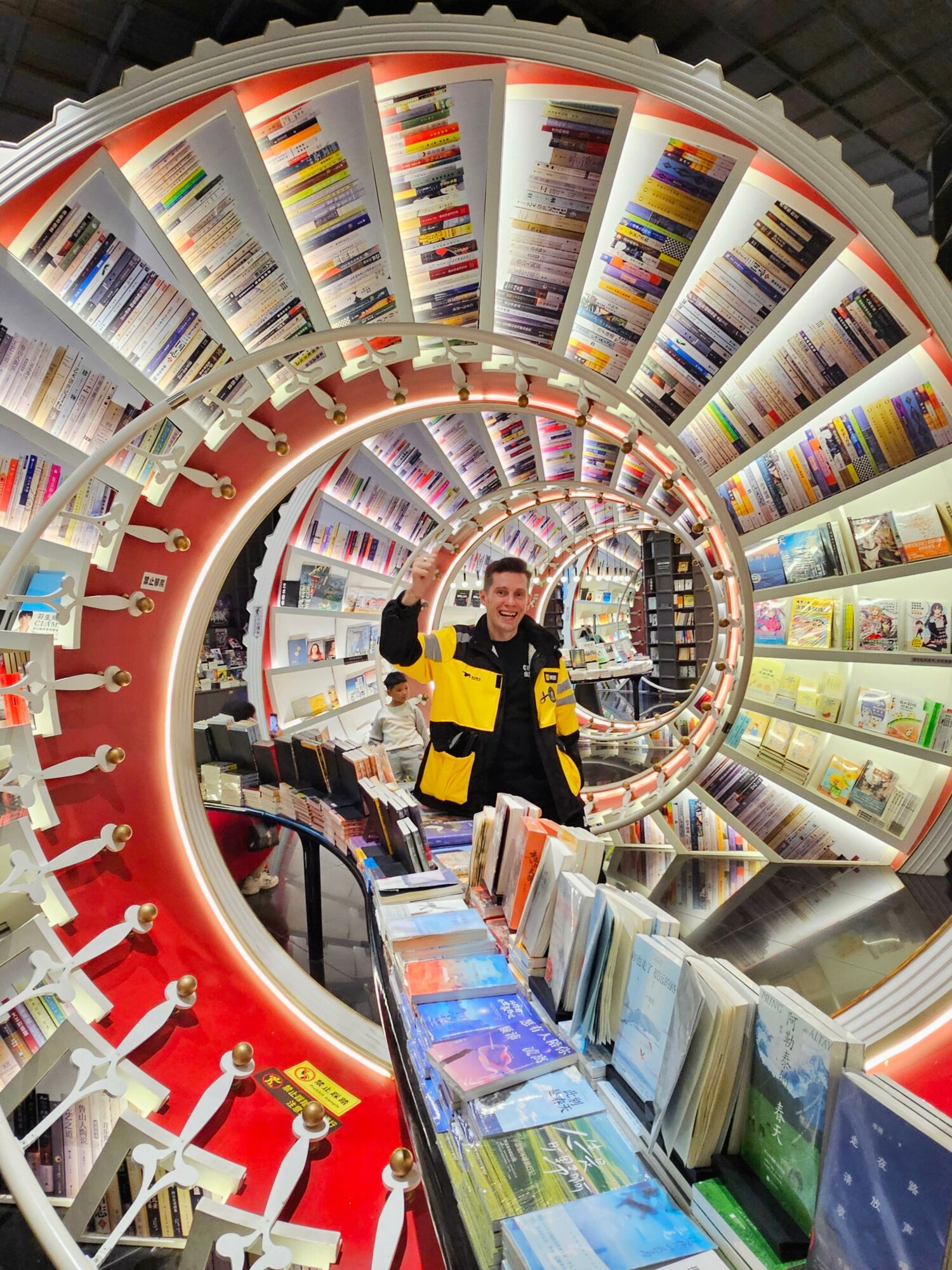 Person in a store aisle with circular shelves filled with colorful books and magazines, smiling and holding a yellow item.