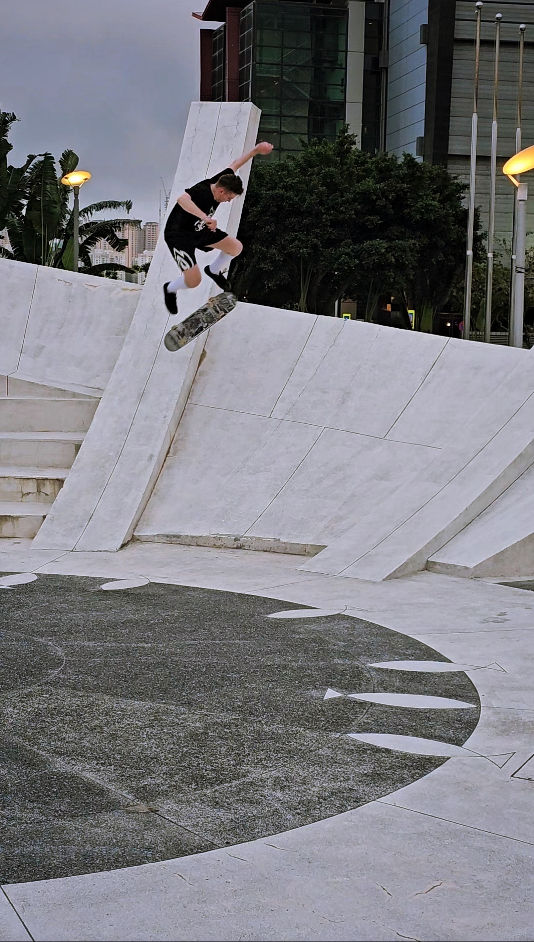 Skateboarder mid-air performing trick on a white concrete structure in an urban park.