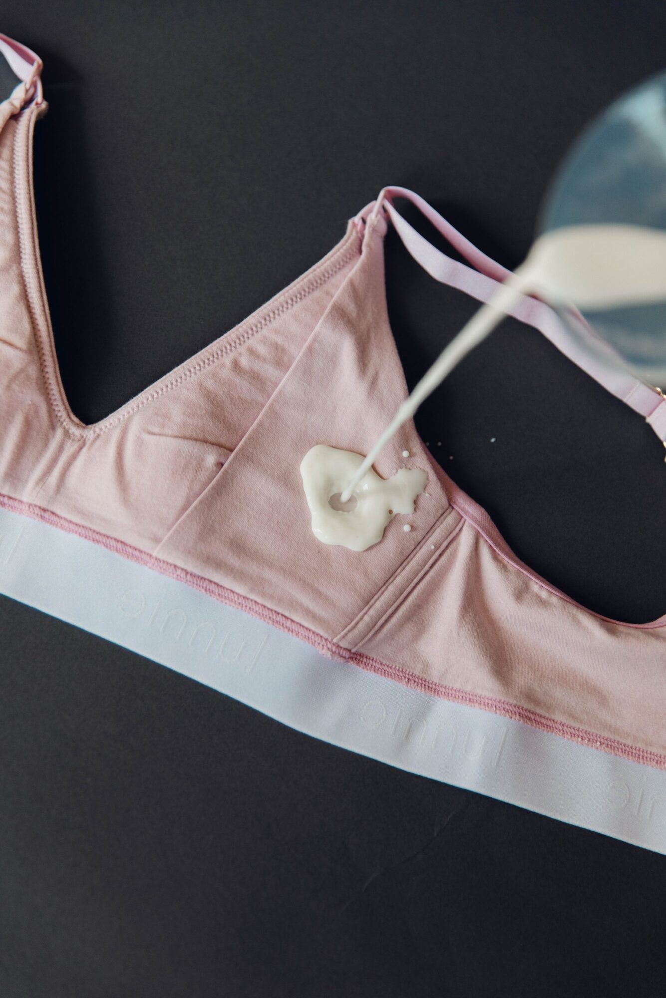 Pink sports bra with white and pink trim, milk being poured onto it, on a black background.