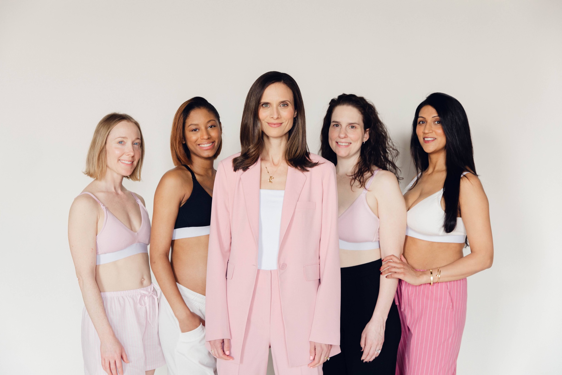 Five women standing together, smiling, in front of a plain white background.