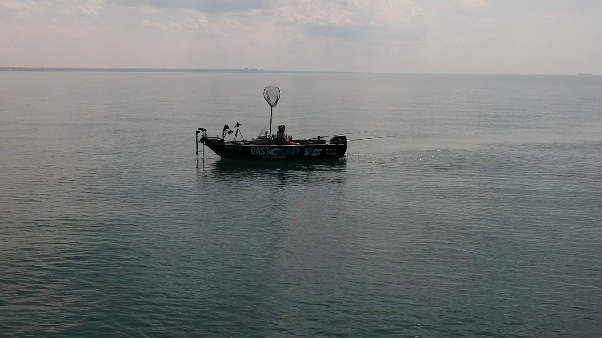 A boat on calm water with a large net or hoop structure on it, under a cloudy sky.