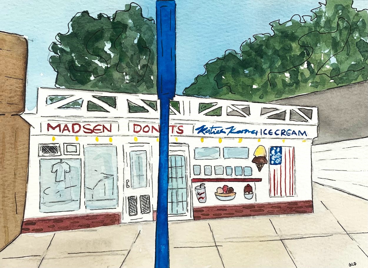 Ice cream shop with signs, ice cream cone, and American flag, trees in background, sidewalk in front.