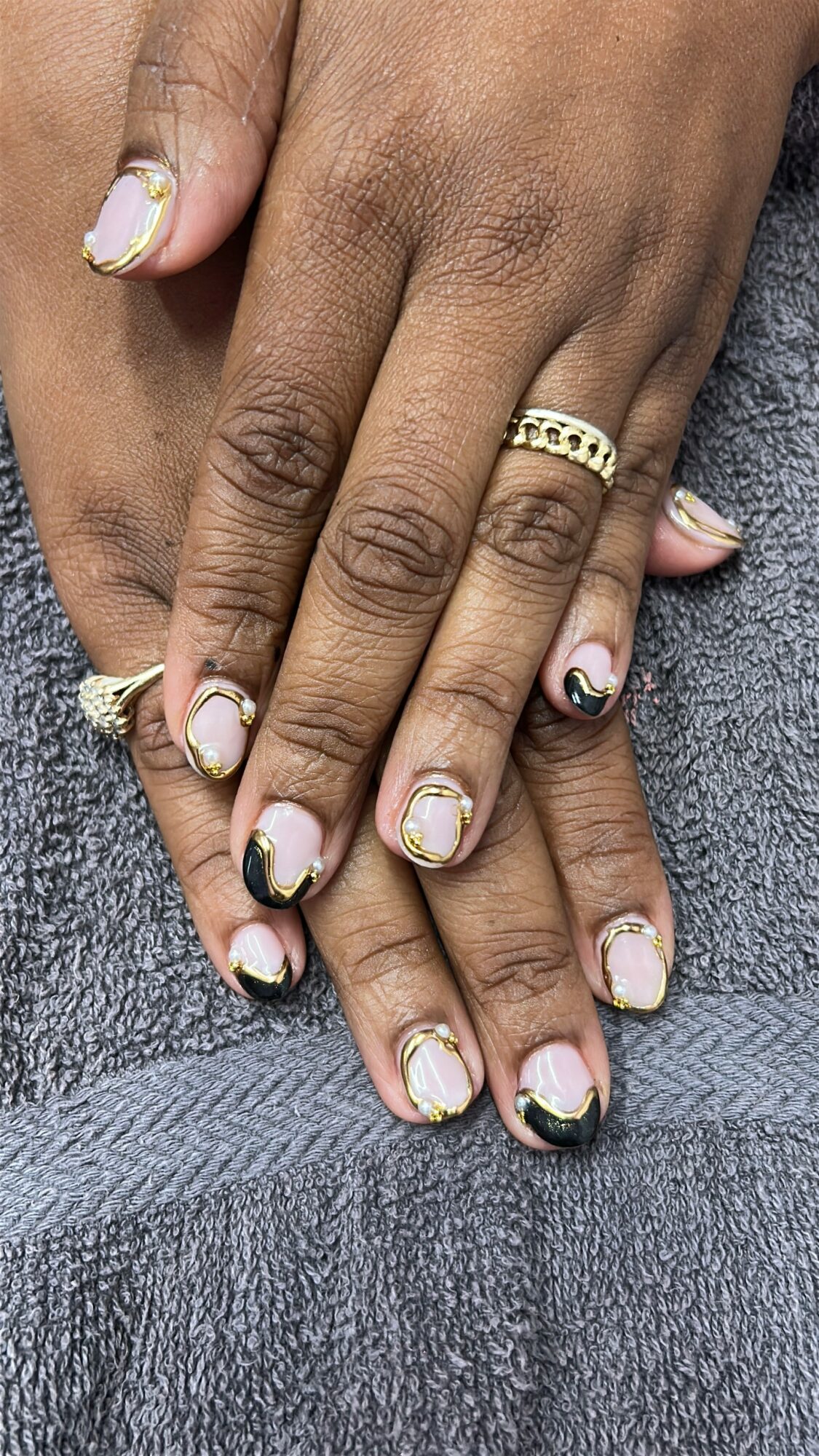 Two hands with decorated nails and rings resting on a gray surface.