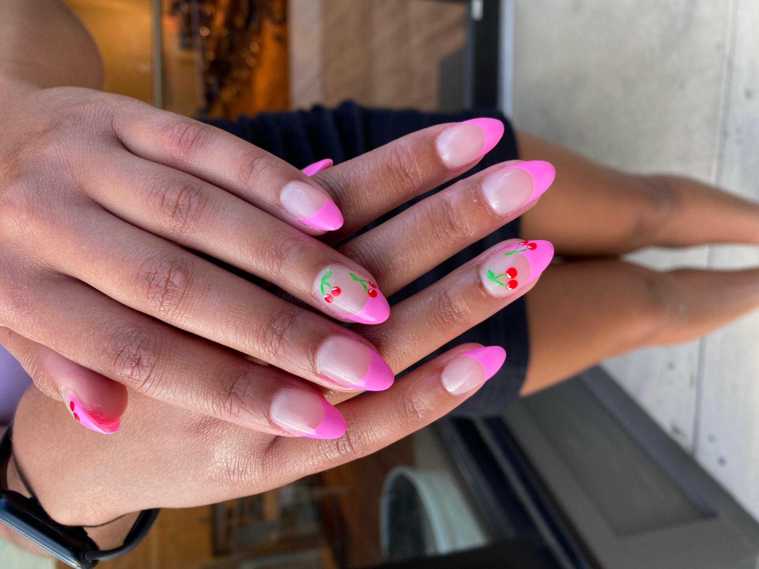 Person's hands with pink and white gradient nails, some decorated with small floral designs, resting on a surface.