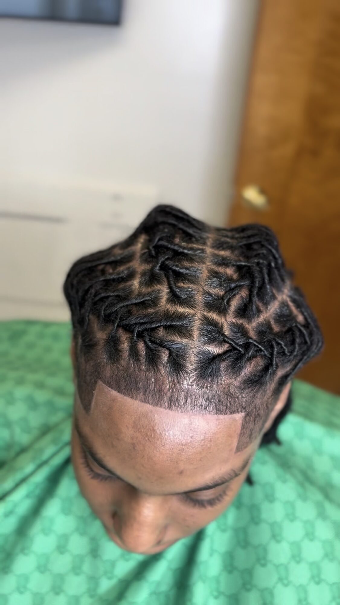 Top view of a person with styled cornrows and a fade haircut, wearing a green patterned shirt.
