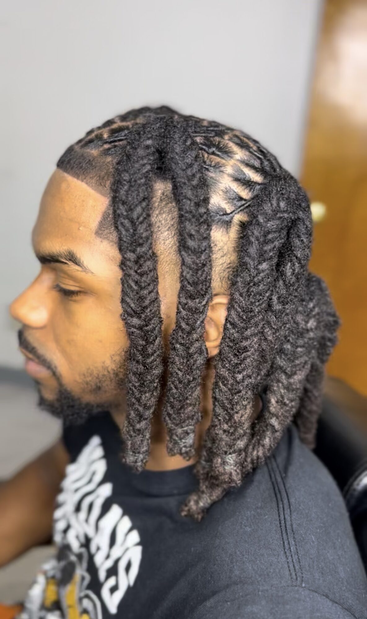 Side view of a person with styled dreadlocks, some shaved on the side, wearing a black shirt.