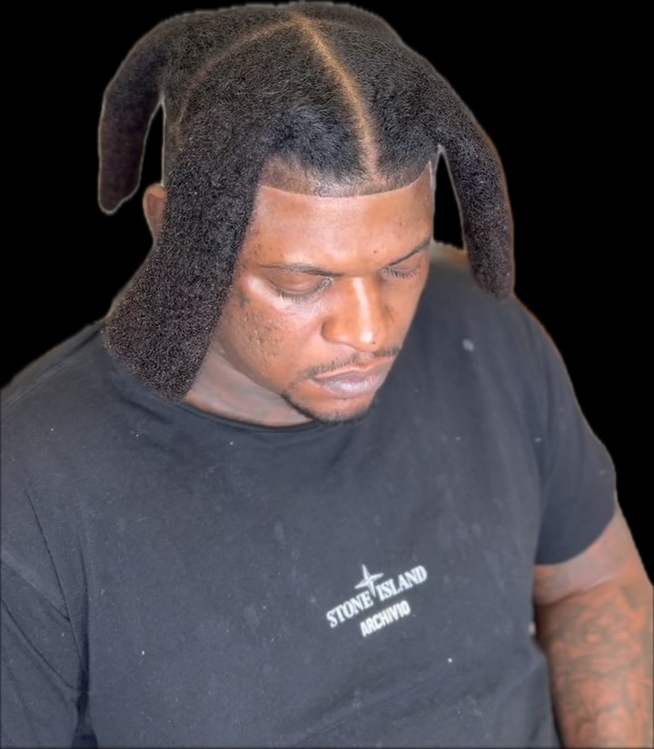 Person with styled hair looking downward, wearing a black T-shirt with white text, against a black background.