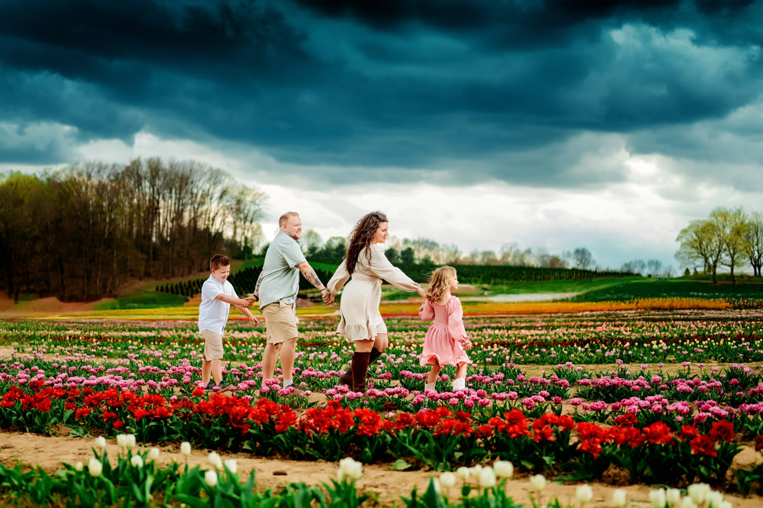 Family of five holding hands in a colorful flower field under a cloudy sky, with trees in the background.