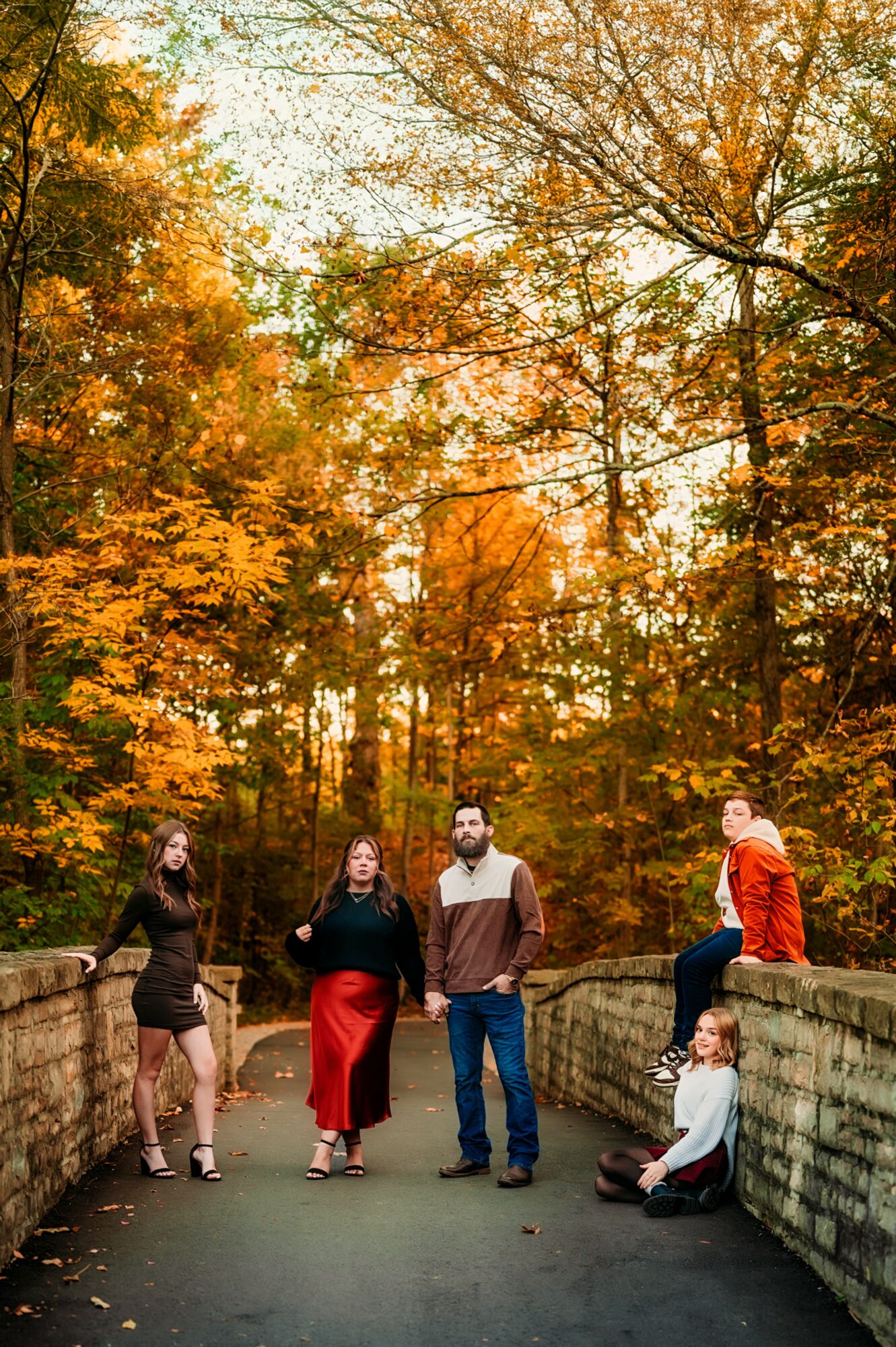 Group of five people standing and sitting on a stone bridge in a forest with autumn leaves.